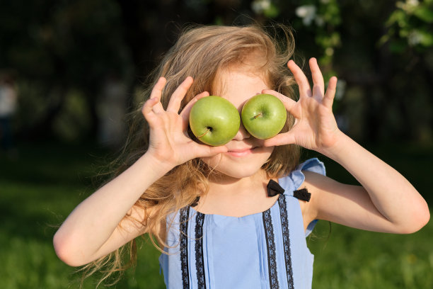 微笑的女孩，拿着苹果在她的眼睛在模糊的绿色花园背景图片下载