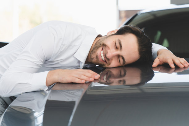 非常高兴的年轻白人商人拥抱他的新车，感觉兴奋后购买昂贵的汽车在汽车经销商商店。图片下载