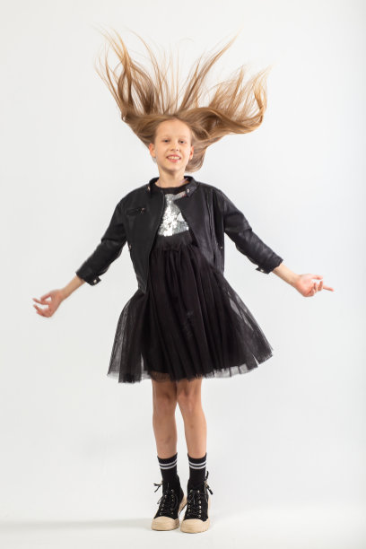 一幅全身跳跃的年轻女孩的肖像，留着棕色长发，穿着流氓风格的衣服。图片下载