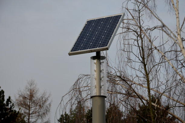 灰色不锈钢圆柱状。这是一盏有透明罩和LED灯泡的灯。在路灯的顶部有一个小的太阳能电池板。公园图片下载