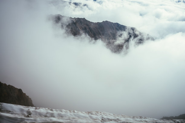 美妙的山景，在浓密的低云中有巨大的岩石。大气山景观与大岩石山之上的云。从白雪皑皑的山顶到高耸的岩石，俯瞰厚厚的云层，美丽的景色。图片下载