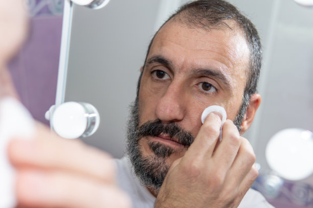 成熟的白种大胡子男子在镜子前用棉花垫洗脸。图片下载