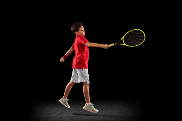 全身像活泼的小男孩，打网球，训练孤立在黑色的背景。图片下载