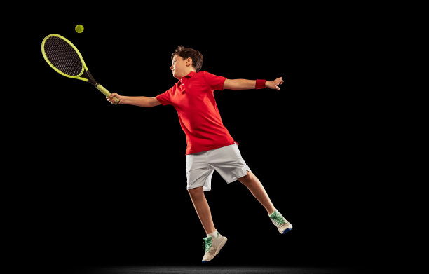 全长肖像的男孩，网球运动员在运动，踢球在一个跳跃在一个孤立的黑色背景图片下载