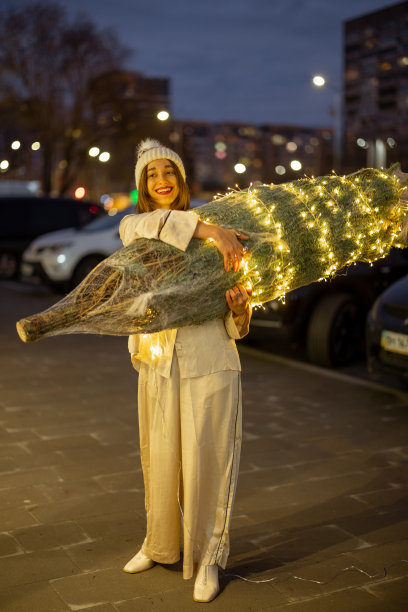 一位妇女在购物中心附近举着彩灯圣诞树图片下载