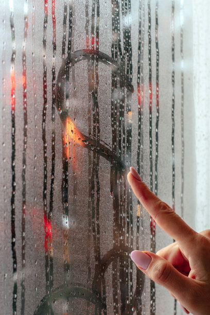 一个女人用手指在雾蒙蒙的窗户上画了一颗心，这是她的手的特写。窗外，圣诞树花环上模糊的灯光。圣诞节和新年的概念。图片下载