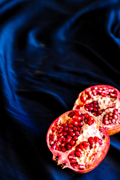 半石榴在黑暗的织物背景。深红色饱和石榴水果在黑色和蓝色丝绸图片下载