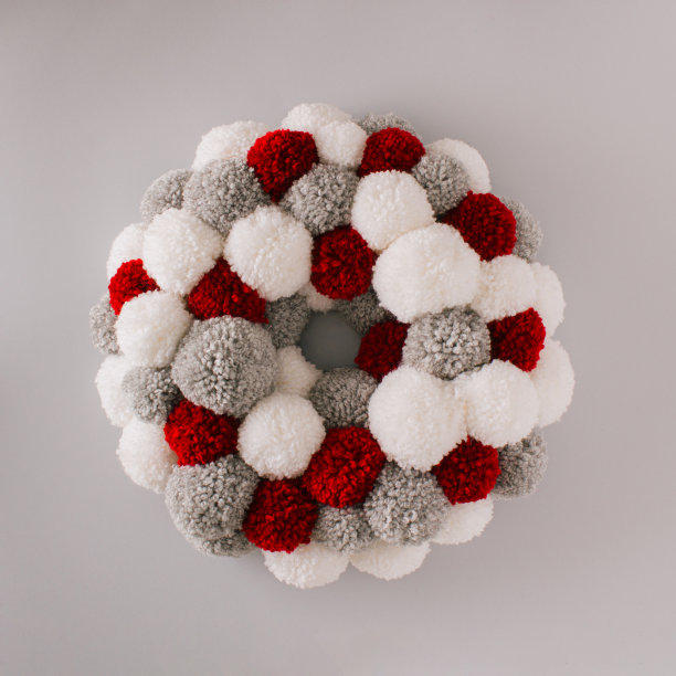 由蓬松的羊毛球制成的圣诞花环。红色、灰色和白色的冬季装饰映衬着银色的背景。最小平铺新年布置。图片下载