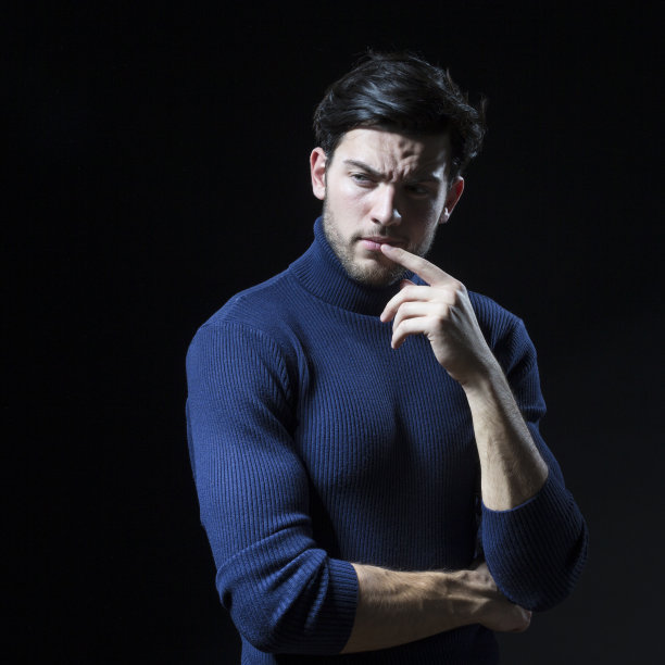 思考英俊的黑发男人摆姿势在蓝色海龟领毛衣与折叠的手在黑色的背景与复制空间作为成功的年轻人。广场形象图片下载
