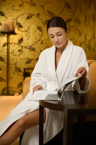 自信有魅力的轻松年轻女子休息在一个健康水疗诊所的休息区，穿着浴袍，阅读杂志，准备接受专业的身体和皮肤护理治疗图片下载