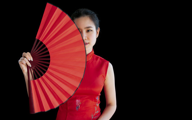 年轻的中国美丽的亚洲女人穿着红色的传统服装，拿着折扇，站在黑色孤立的背景剪纸，看着相机，微笑着庆祝新年与复制空间。图片下载