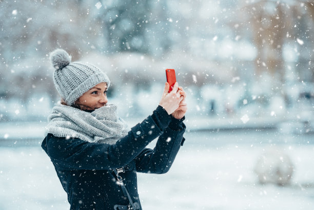 一名女子在寒冷的冬天戴着围巾和帽子，用智能手机自拍图片下载