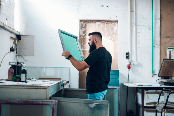 在一个印刷车间里，男工人拿着丝网框架图片下载