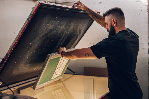 在印刷车间工作时使用屏幕曝光设备的男性工人图片下载