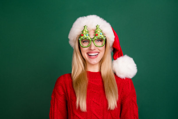 照片迷人有趣的年轻女士戴红色毛衣头饰树眼镜微笑孤立的绿色背景图片下载