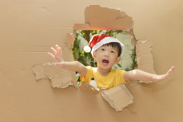可爱的小男孩戴着圣诞帽，在破墙纸墙上摊开他的手图片下载