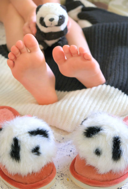早上在家里闭上光脚，放松。有趣的毛绒熊猫拖鞋。舒适的美学风格图片下载