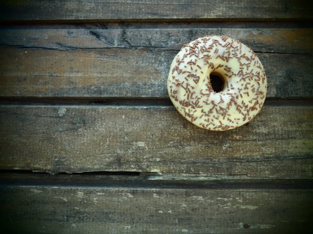 木制背景上的甜甜圈特写。有香草糖霜和巧克力点缀的美味蛋糕。高热量的早餐或零食。香草、巧克力、甜甜圈或生面团甜点图片下载