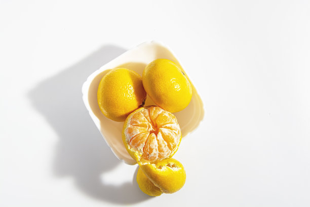 两个完整的橘子和一个半剥皮放在一个方形的白色碗里，背景是白色的。隔离。特写镜头。水平的照片图片下载