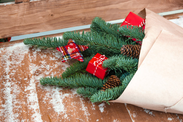 冬天用杉木枝纸制成的花束，饰以球果，礼品红盒。花束放在一张木凳上，上面覆盖着雪。圣诞节和新年的概念。图片下载