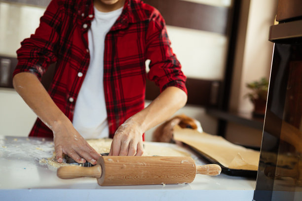 孩子的手从面团中切饼干的特写。穿着围裙的男孩把饼干切成动物形状。擀面杖,表。面粉。的爱好。图片下载