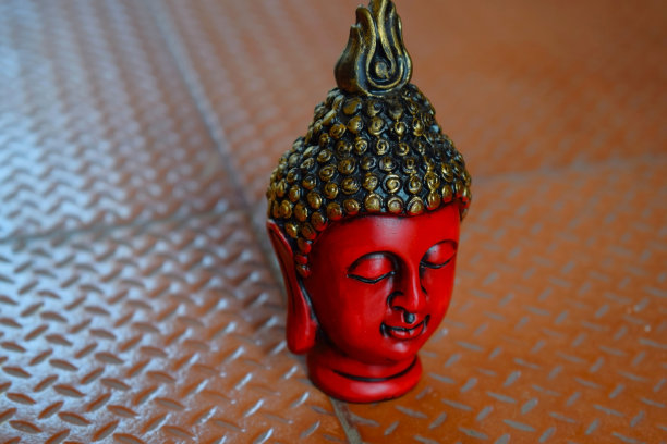 库存照片美丽的红色脸雕塑或佛陀的雕像，雕像的头涂上黑色和金色在棕色的背景上，图片捕获在印度班加罗尔。图片下载
