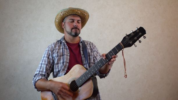 一个戴草帽，穿格子衬衫的男人。他手里拿着一把古典吉他图片下载