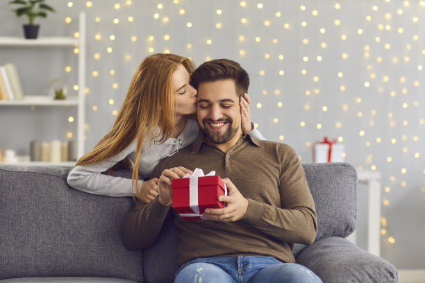 在这个特别的日子里，一名女子从后面拥抱并亲吻她心爱的丈夫，并送给他一份礼物。图片下载