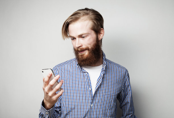 大胡子男子看着智能手机屏幕的特写照片图片下载