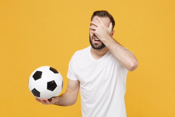 沮丧的年轻大胡子球迷穿着白色t恤孤立在黄色背景。人们运动家庭休闲理念。用手捂着脸，用足球鼓励支持喜欢的球队。图片下载