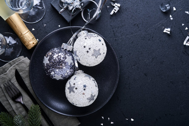 圣诞桌设置黑色的圣诞冷杉树枝，圣诞银球和香槟，眼镜在黑色的背景上圣诞问候。圣诞快乐，新年快乐的概念图片下载