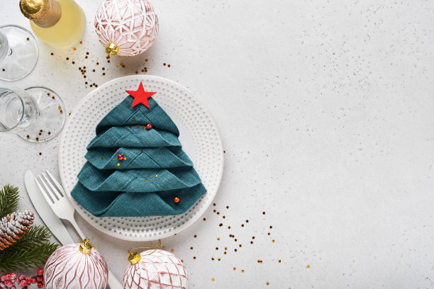 圣诞餐桌设置白色与黑色银器，折叠成圣诞树的餐巾，圣诞银球，香槟，白色背景的圣诞问候眼镜。为文本腾出空间。图片下载