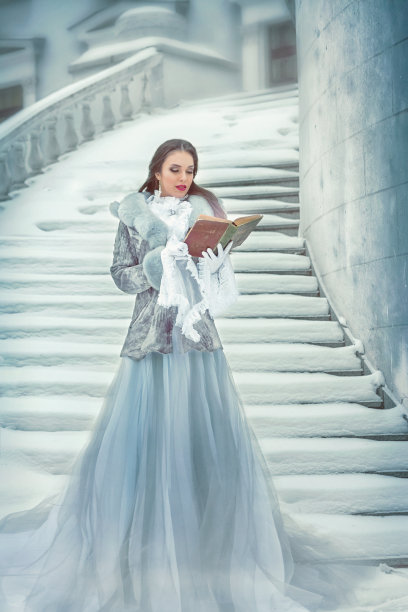 在一幅历史图片中，一位美丽的黑发女子在冬天的雪地里站在白色的大楼梯上看书。图片下载