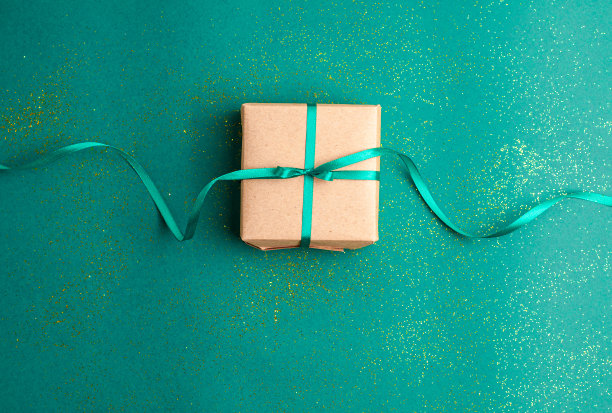 棕色的礼品盒与翠绿色缎带蝴蝶结在绿色的背景与金色的闪光。圣诞假期和现在的概念平lay。图片下载