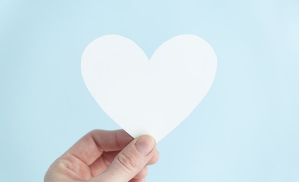 手拿着一颗蓝色背景下的白心。慈善，纯爱，慈悲善良的理念。前视图。图片下载