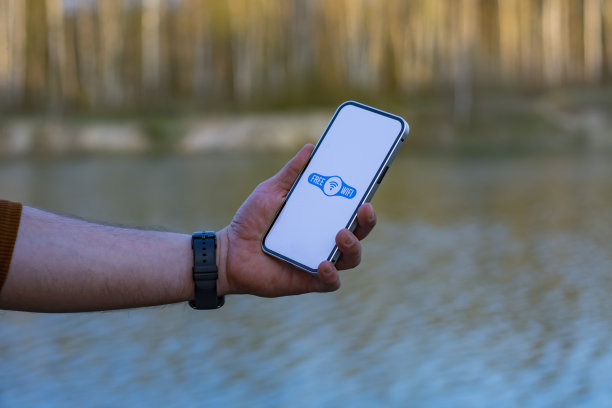 一名男子手里拿着智能手机，屏幕上有一个免费的wi-fi图标。手机背景是森林和湖泊。自然的免费互联网接入。图片下载