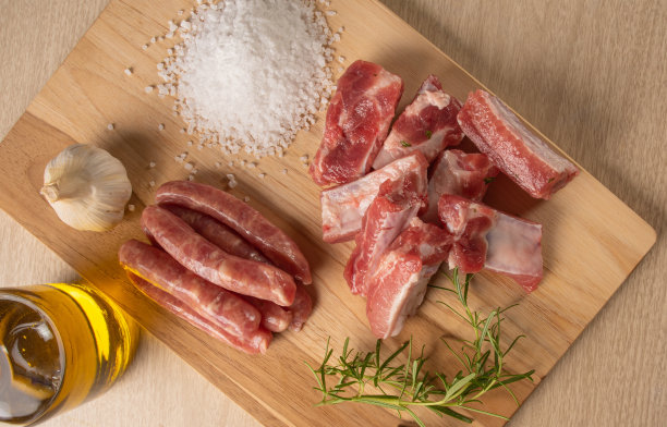 猪排、香肠、岩盐、大蒜、洋葱、迷迭香和橄榄油放在桌子上，俯视图。图片下载