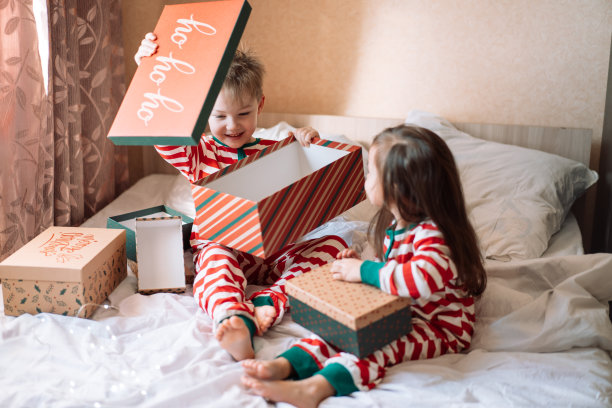 穿着睡衣的孩子们坐在白色的床上打开圣诞礼物图片下载