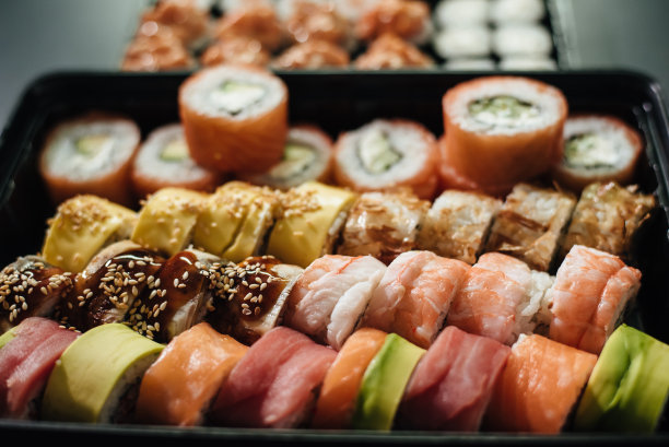 日本食品的概念。餐饮，各式寿司上碟。放置在石黑色背景的塑料输送盒。寿司卷(费城)，三文鱼，烟熏鳗鱼，鳄梨，奶油芝士。图片下载