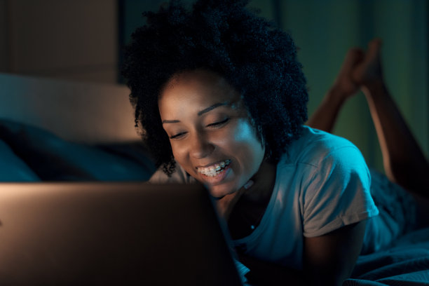 快乐的女人躺在床上，用笔记本电脑看电影图片下载