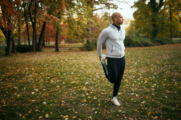 年轻的非洲裔美国跑步者在秋天公园慢跑前伸展他的腿。图片下载