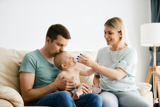 年轻的父母在家里给孩子喝水时用奶瓶。图片下载