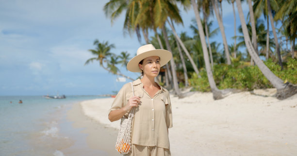 正面照片是一个深色皮肤的女人，穿着狩猎装，戴着帽子，走在空荡荡的热带海滩上图片下载