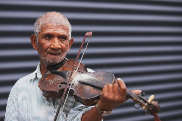 近距离的照片，一个头发花白、没有刮胡子的老人音乐家拿着一把木制小提琴，在户外演奏着美丽的旋律。图片下载