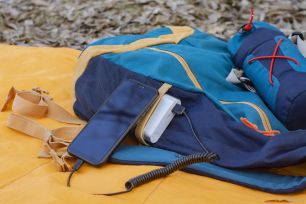 这款智能手机正在使用便携式充电器充电。一个带手机的动力银行，一个带背包的睡袋。图片下载