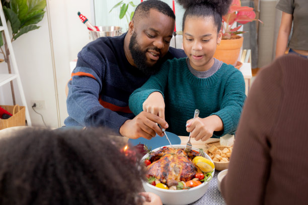 父亲和女儿用刀切火鸡肉烤在盘子上一起在家里吃，感恩节前夕，庆祝圣诞节与家人一起吃饭，新年，圣诞节假期。图片下载