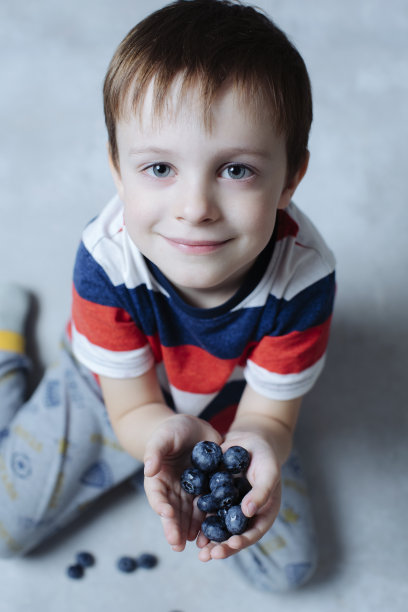 天真微笑的好孩子手里拿着蓝莓。健康洁净营养理念图片下载