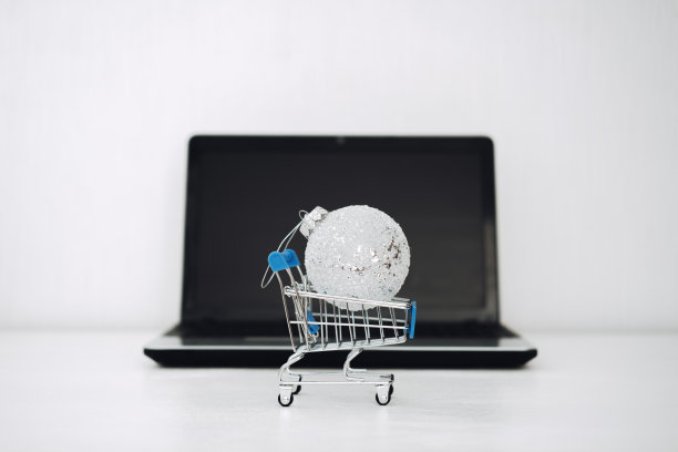 圣诞网上购物，冬季大减价，黑色星期五。圣诞装饰品玩具球在购物车黑色笔记本电脑黑屏背景。图片下载