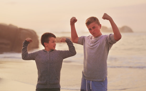 两个年轻的兄弟站在海滩上秀肌肉的裁剪肖像图片下载