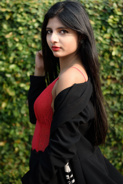 肖像非常美丽的年轻有吸引力的女人穿着红色的衣服和黑色的夹克摆时尚在一个模糊的绿色背景。生活方式和时尚。图片下载